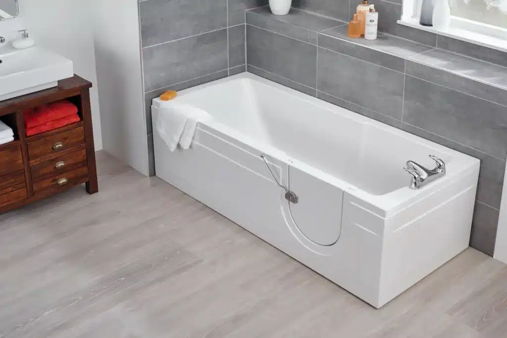 Modern bathroom with a sleek white bathtub, wooden vanity, gray tiles, and light wood flooring.