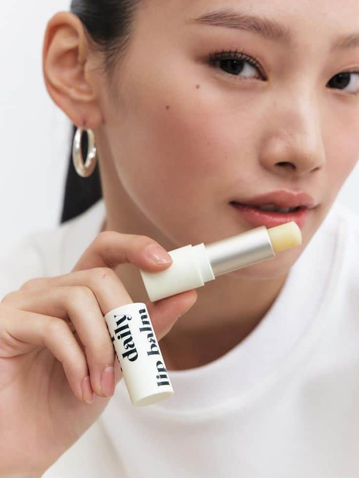 Woman holding a tube of daily lip balm, showcasing soft, natural lip care product.