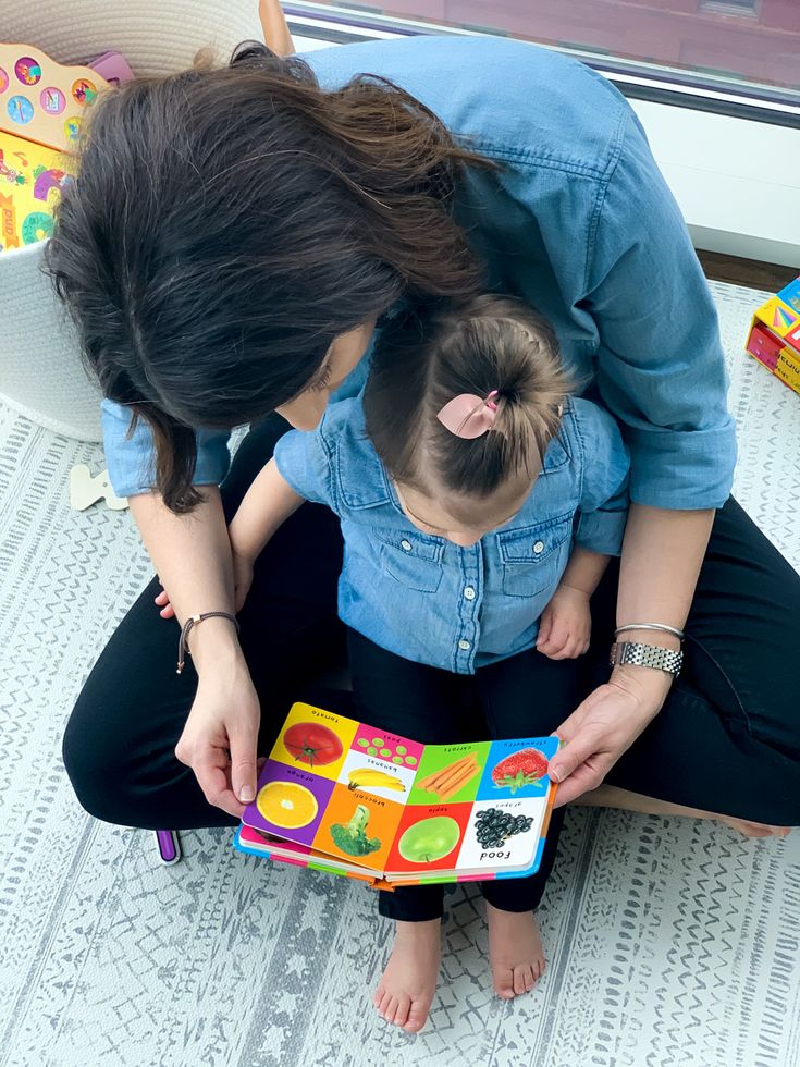 Mother and child reading a colorful children's book on a patterned rug.