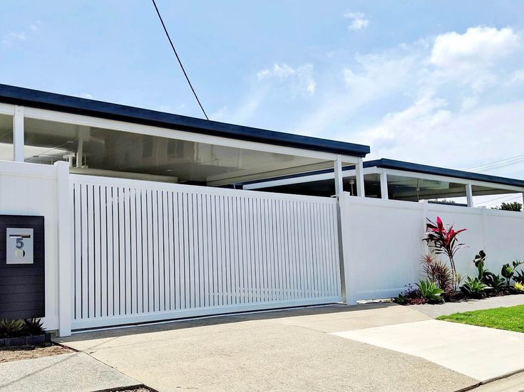 Modern white fence with gate and driveway, house number 5, blue sky background.