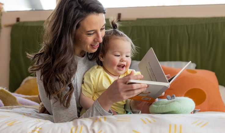 Mother and toddler reading a book together on a cozy bed, smiling and enjoying family time, engaging in early learning. Best Indoor Games for Toddlers