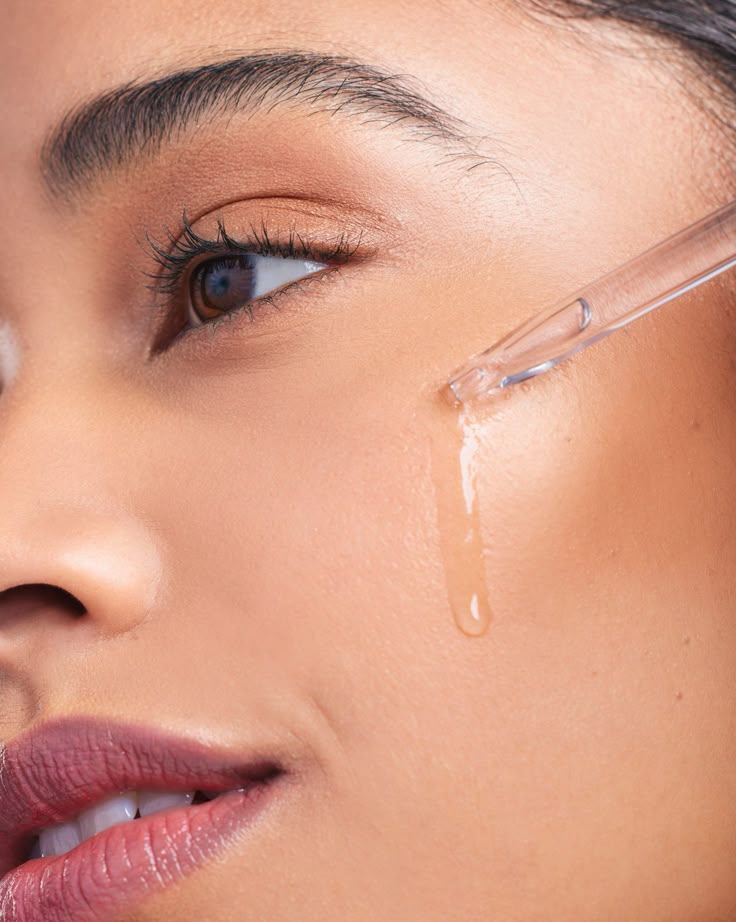 Close-up of a woman applying face serum with a dropper on her cheek for skincare routine.