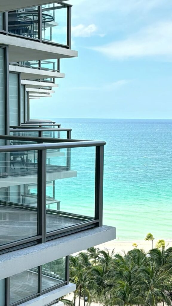 Modern glass balconies overlooking a serene ocean view with palm trees and a clear blue sky.