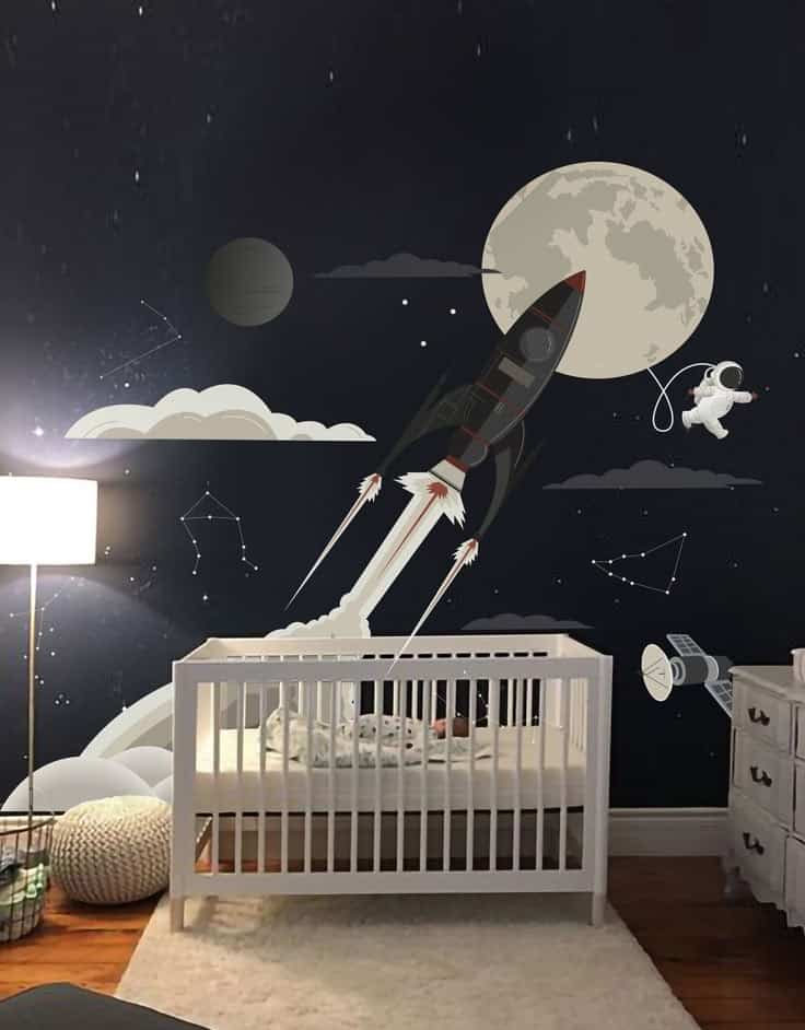 Space-themed nursery with crib, rocket, astronaut, and moon mural on dark wall, creating a dreamy atmosphere.