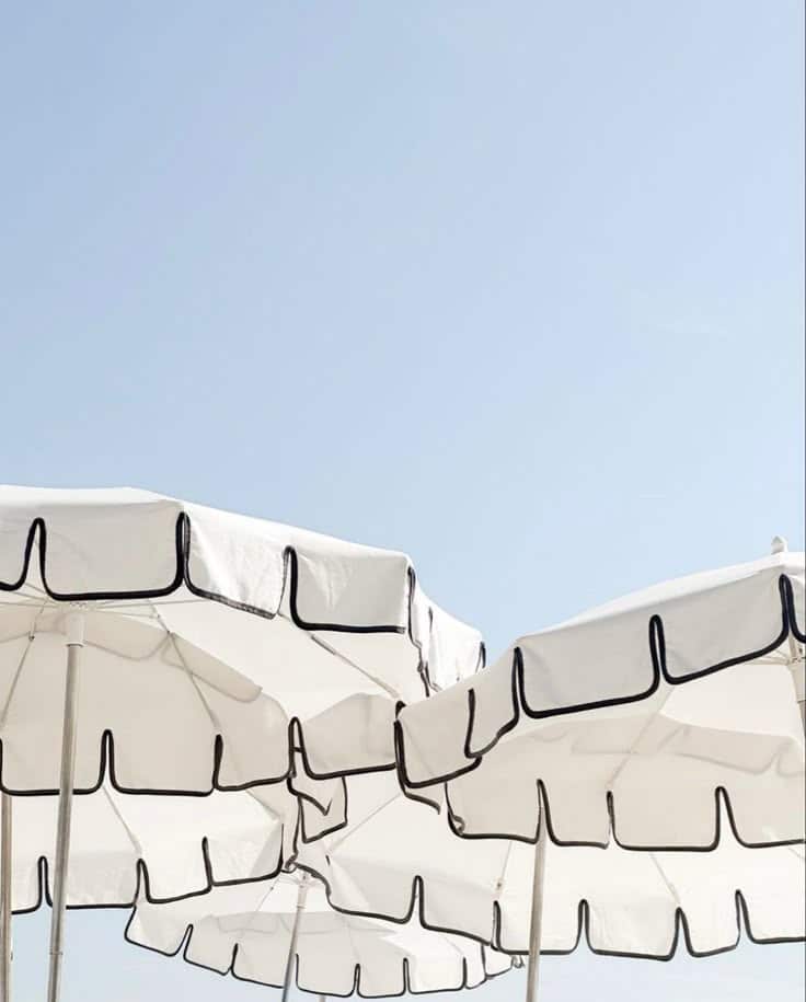 White beach umbrellas with black trim against a clear blue sky, creating a minimalist summer scene.