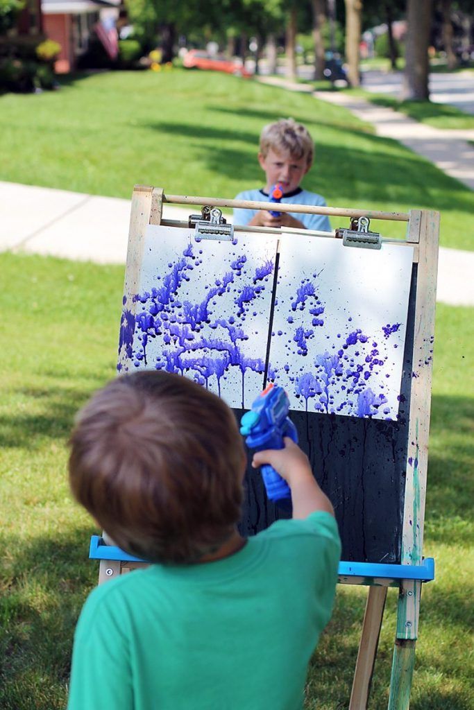 Children using water guns to create splatter art on canvas outdoors.