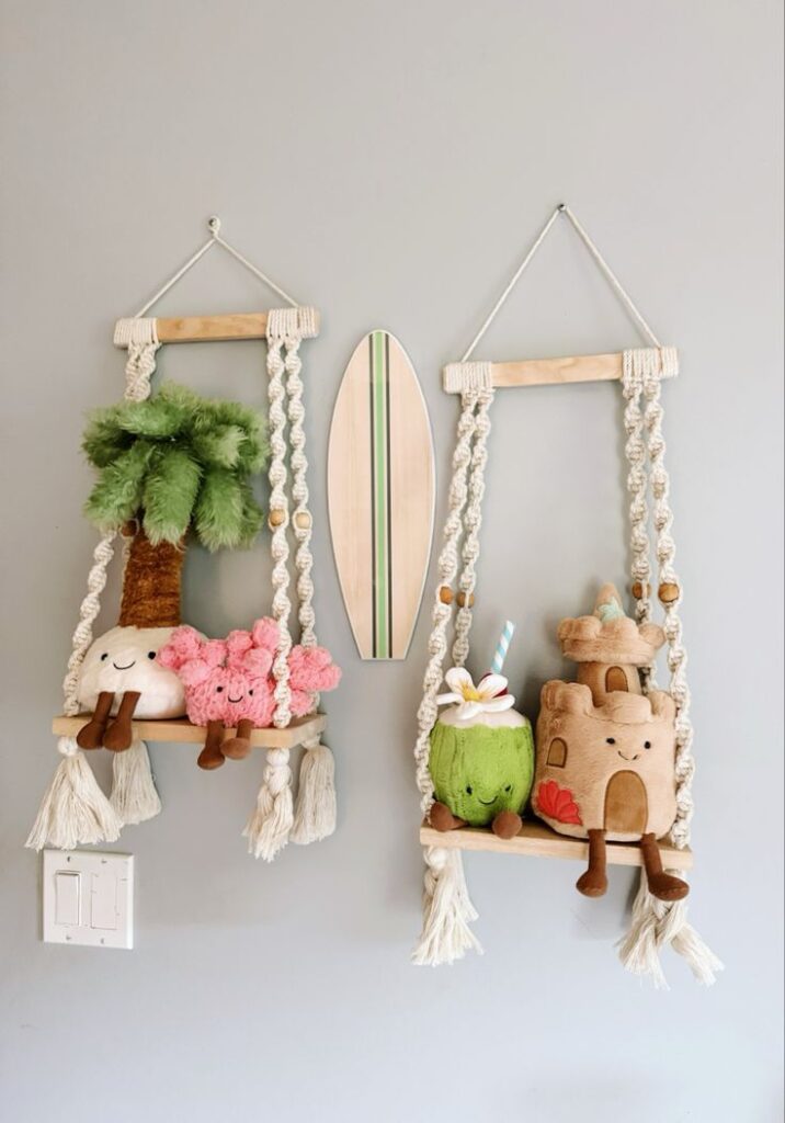 Whimsical plush toys on macramé swings with surfboard decor on a gray wall. Boho nursery decor idea.
