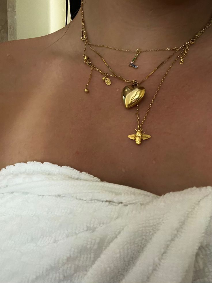 Golden layered necklaces with heart and bee pendants on woman's neck, wrapped in white towel.
