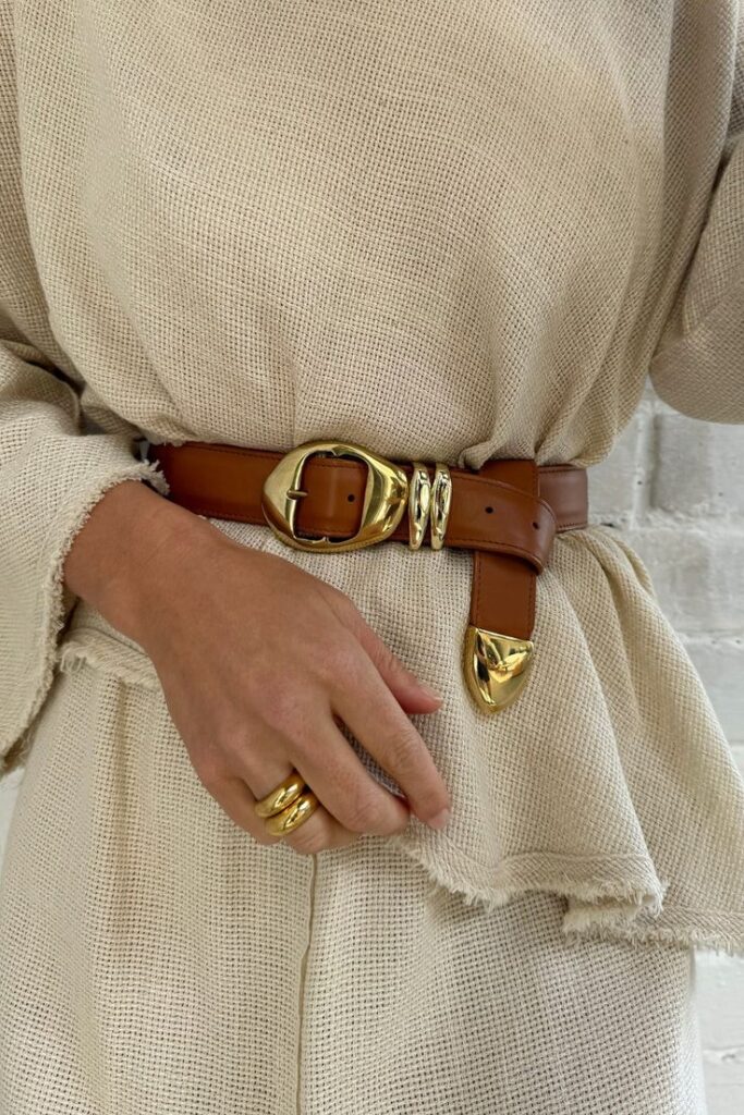 Fashionable beige dress with a brown belt and gold accents. Elegant style with matching gold rings.