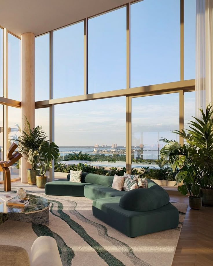 Modern living room with large windows, green sofa, lush plants, and stunning ocean view. Bright and spacious interior design.