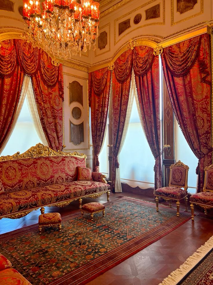 Luxurious room with ornate red and gold furnishings, intricate patterned carpet, and grand chandelier.
