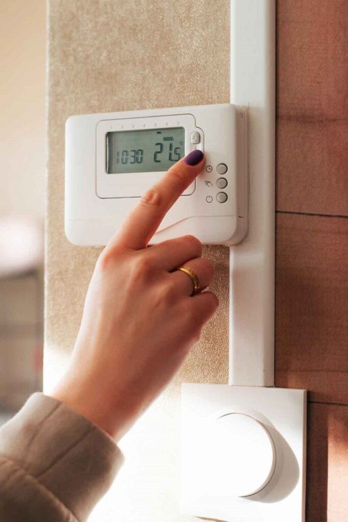 Person adjusting a digital thermostat on a wall for home temperature control.