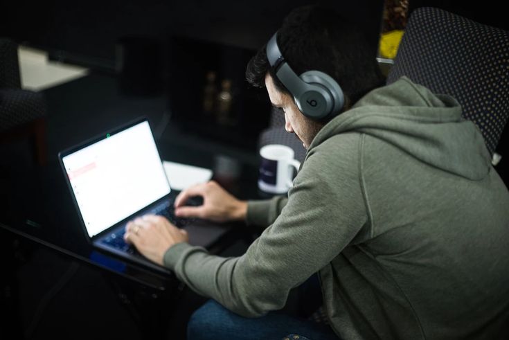 Man wearing headphones working on a laptop with a coffee mug nearby.