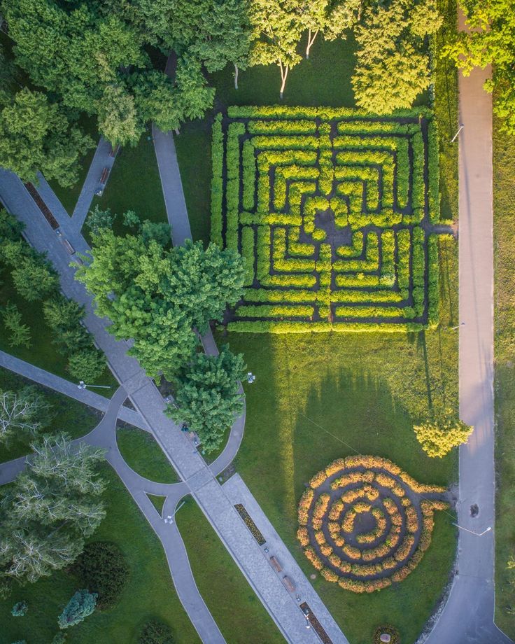 Aerial view of lush green maze and spiral garden in a park with intersecting paths and surrounding trees.