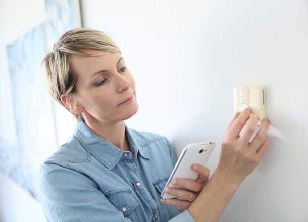 Woman adjusting thermostat with smartphone app for smart home climate control.