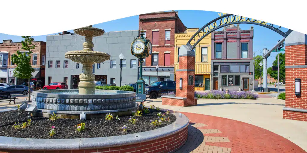 Tipton Place-1 Historic town square with a decorative fountain, vintage clock, and charming storefronts under a bright blue sky. | Sky Rye Design Historic town square with a decorative fountain, vintage clock, and charming storefronts under a bright blue sky.