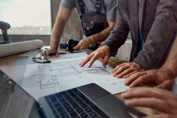 Architects reviewing blueprints at a conference table with a laptop in a modern office setting.