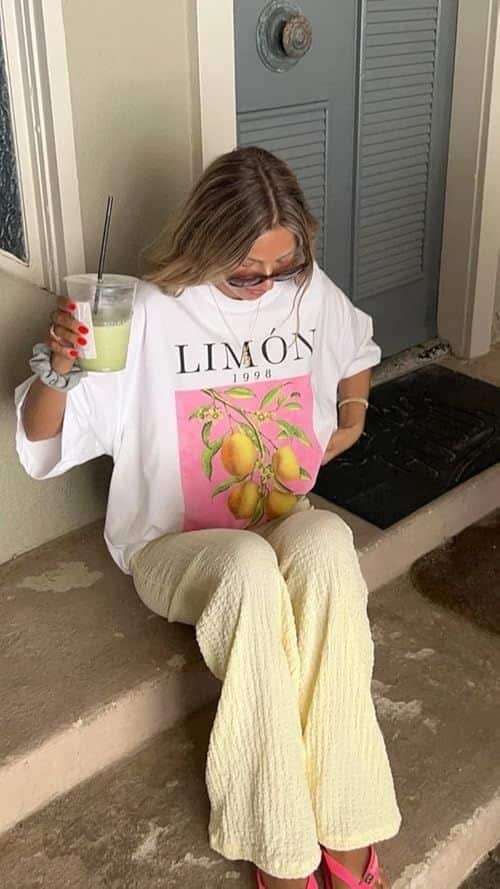 Person wearing a lemon-themed shirt, holding a drink while seated on a step.