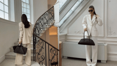 Stylish woman in a white suit holding a black tote bag on stairs and in a sunlit room.