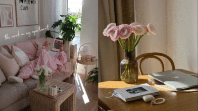 Cozy living room with pink decor, flowers, and a laptop on a wooden table. Bright, airy space with natural light.