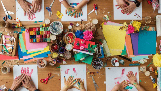Hands painting and crafting on a table filled with colorful art supplies, papers, paints, and scissors.