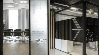Modern office interior with a glass-walled meeting room and stylish black chairs, featuring sleek design elements.