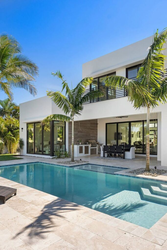 Modern luxury home with palm trees and swimming pool under clear blue sky.