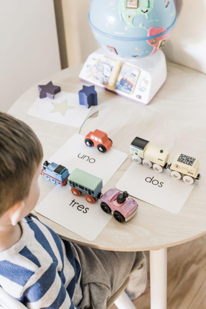 Child learning numbers with toy cars and flashcards in Spanish on a table with globe and stars.