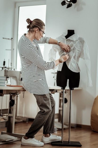 Young designer working in his studio _ Premium Photo Designer adjusting a garment on a mannequin in a studio with sewing machines. | Sky Rye Design Designer adjusting a garment on a mannequin in a studio with sewing machines.