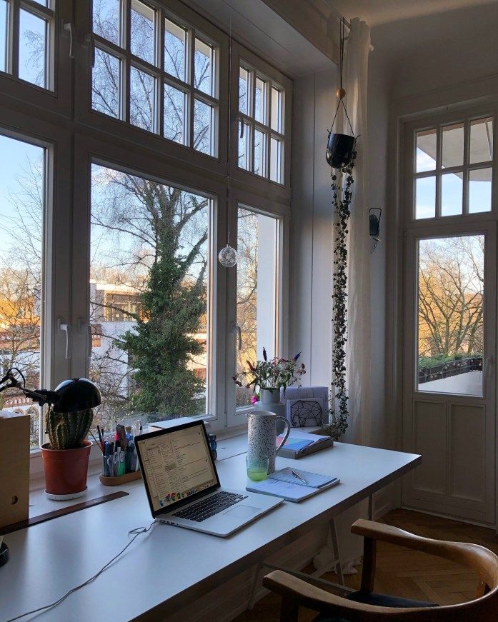 Bright home office with laptop, large windows, plants, and sunny view. Perfect workspace inspiration.