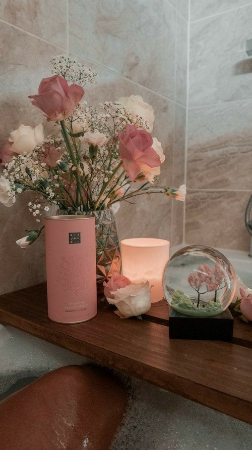 Cozy bath setup with flowers, candle, and decorative globe on wooden tray, creating a relaxing spa-like atmosphere.