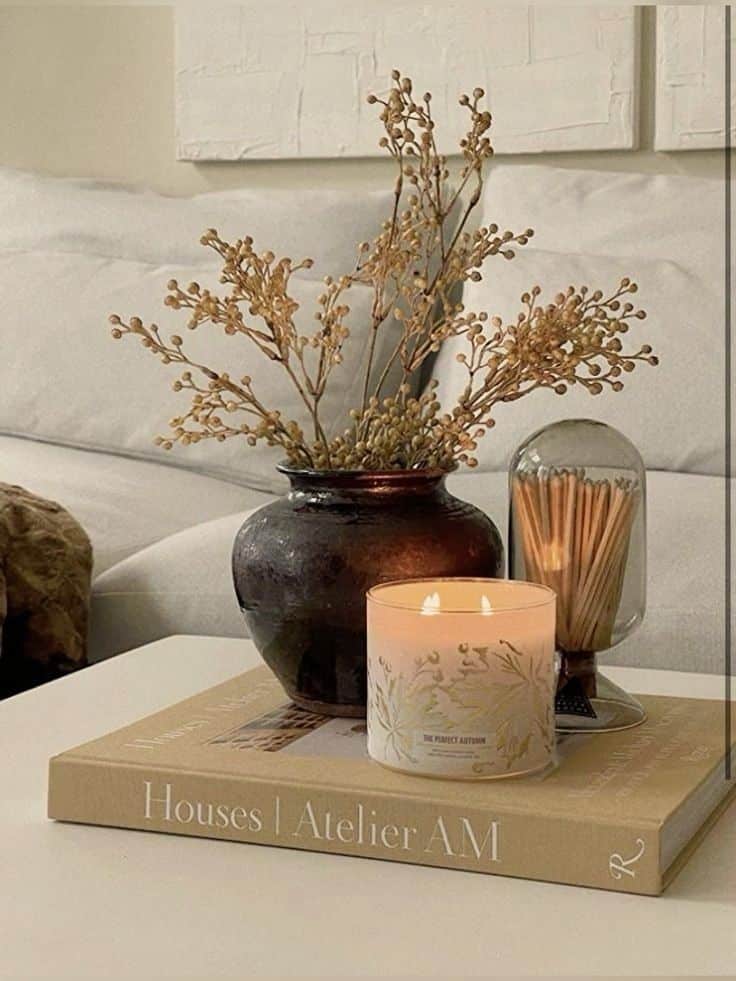 Cozy living room scene with candle, dried flowers in dark vase, and matchsticks on a coffee table book.