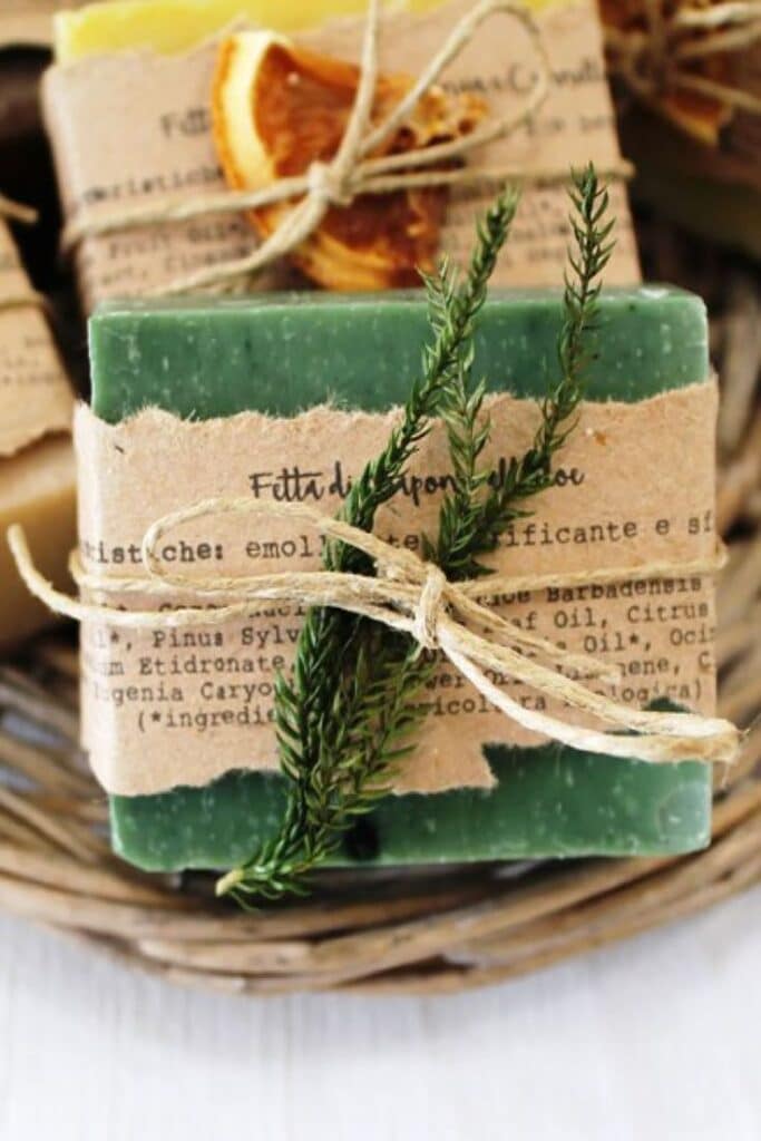 Homemade green soap bar wrapped in rustic paper and twine, adorned with rosemary, in a woven basket.