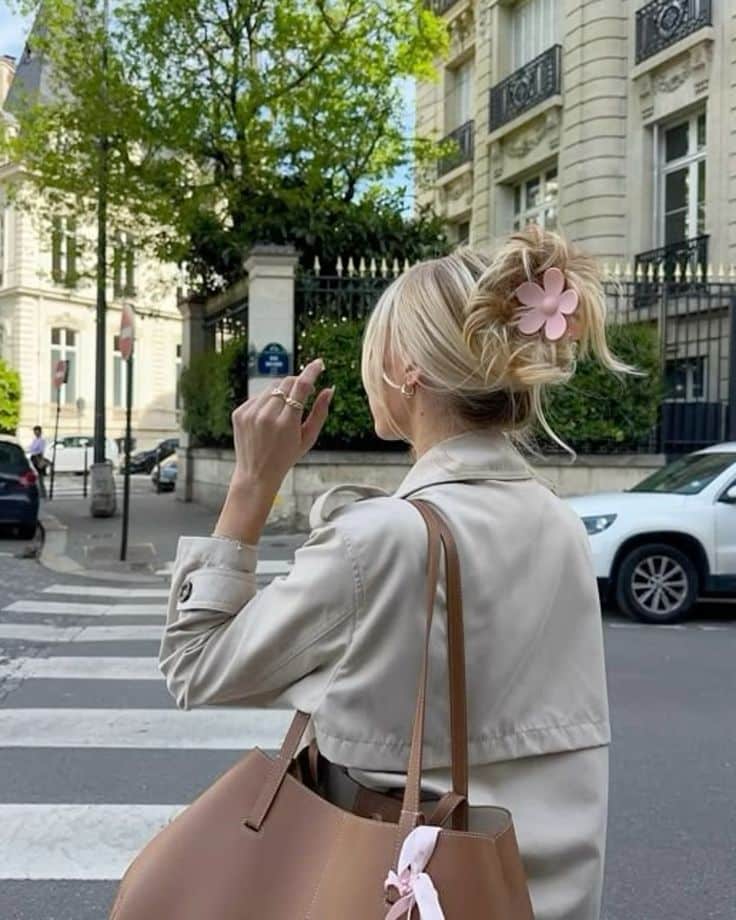 Fashionable woman with trench coat and handbag crossing street in cityscape.
