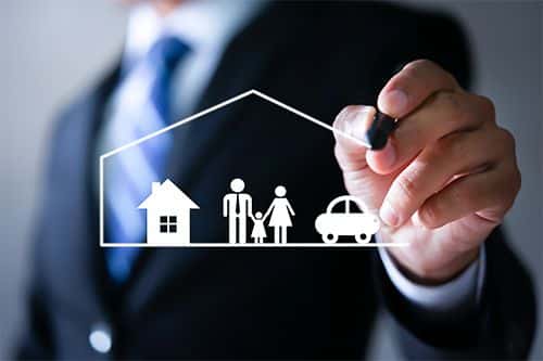 Businessman drawing a house shape encompassing a family and car, symbolizing home and life insurance protection.
