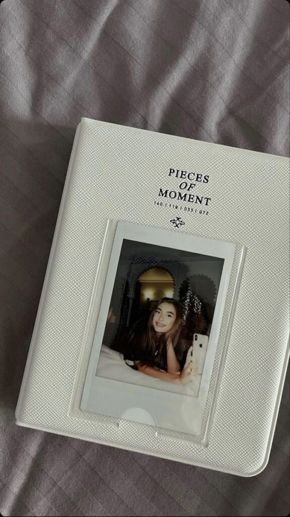 White album titled 'Pieces of Moment' on bed with a smiling photo inside.