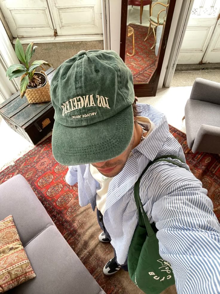 Man with green Los Angeles cap and striped shirt in stylish room with red rug and plants.