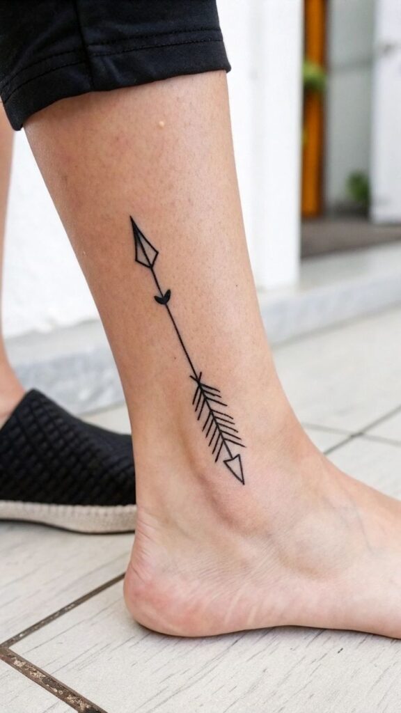 Minimalist arrow tattoo on ankle, black line design on skin, casual footwear in background.