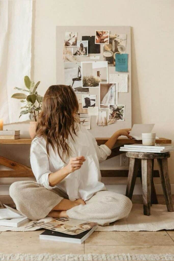Woman creating mood board with photos and textures, seated on floor in cozy, creative workspace.