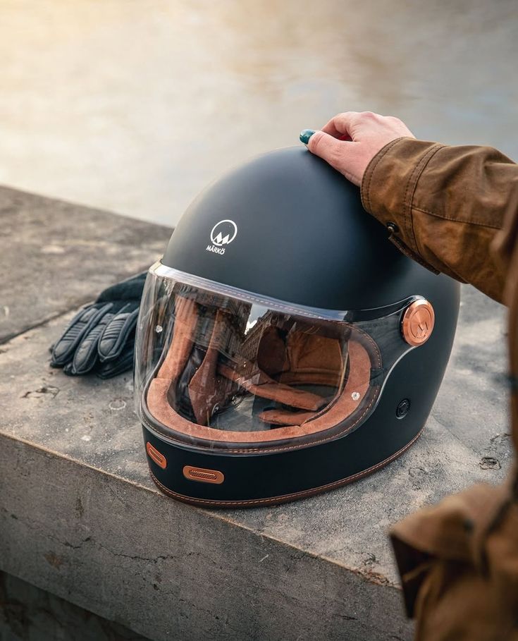 Sleek black motorcycle helmet with visor on a ledge, gloved hand touching it, outdoors setting.