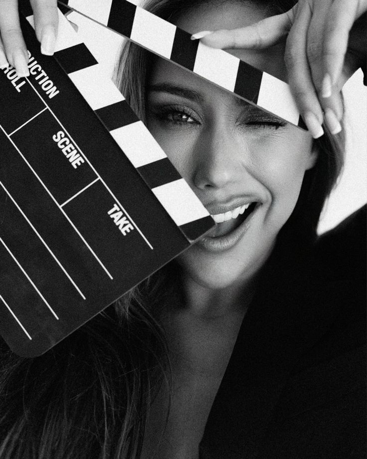 Woman winking behind a film clapperboard, ready for action on a movie set in black and white style.