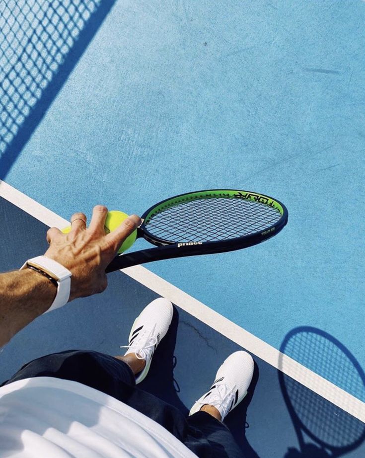 Person holding a tennis racket and ball on a blue court, wearing white shoes and wristband, ready to play.