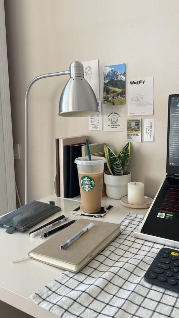 Modern workspace with laptop, lamp, iced coffee, notebook, and plant on tidy desk.