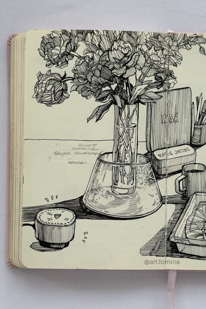 Black ink drawing of flowers in a vase on a desk with an iPad, notebook, and mug. Sketch by @art.fomina.