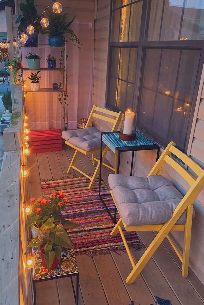 Cozy balcony with yellow chairs, vibrant plants, a colorful rug, and string lights creating a warm, inviting atmosphere.