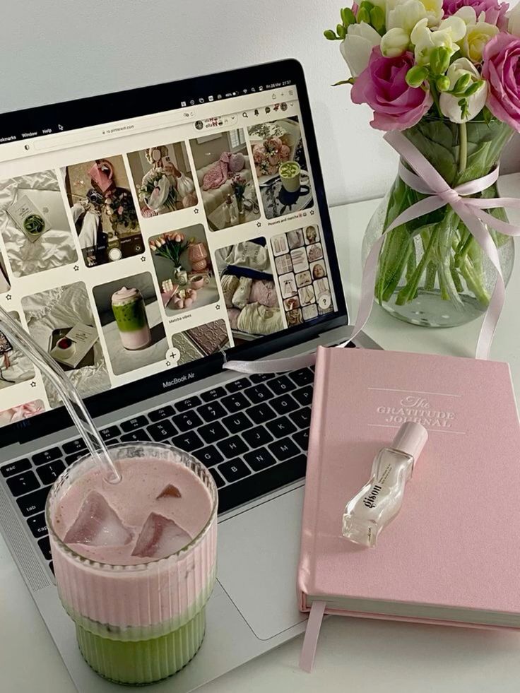 Laptop with Pinterest, pink journal, iced drink, and flowers creating a cozy workspace vibe.