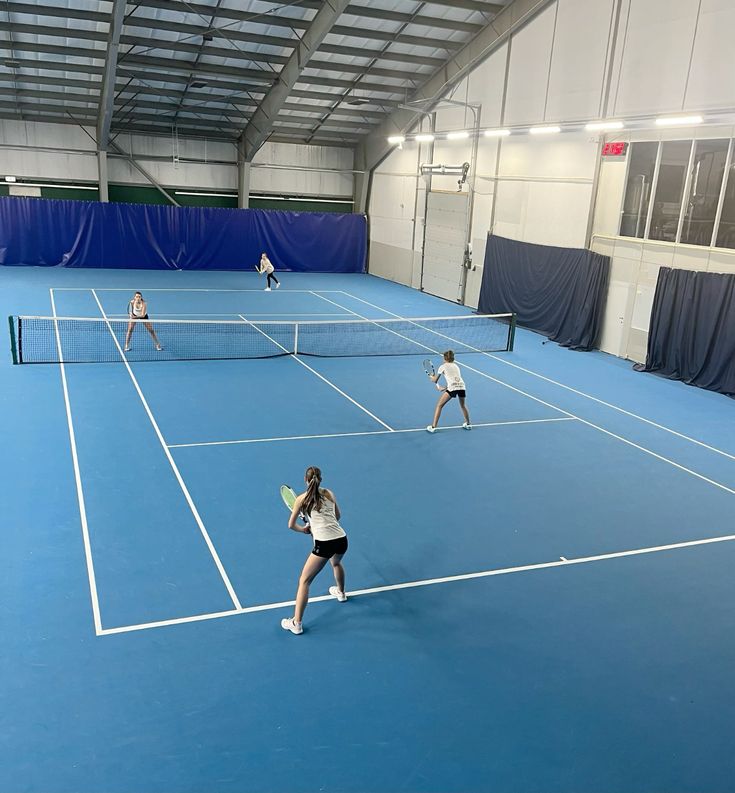 Indoor tennis doubles match in action with players engaged on a blue court.
