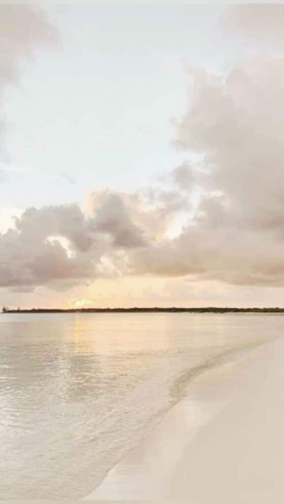 Serene beach at sunset with gentle waves and cloudy sky, creating a tranquil and soothing coastal landscape.