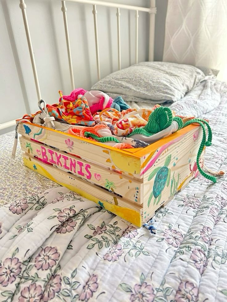 Colorful bikinis in a decorated wooden box on a floral quilted bedspread.