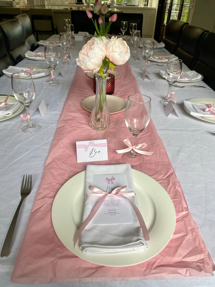 Elegant table setting with pink runner, flowers, and ribbon-tied napkins. Romantic dining ambiance.
